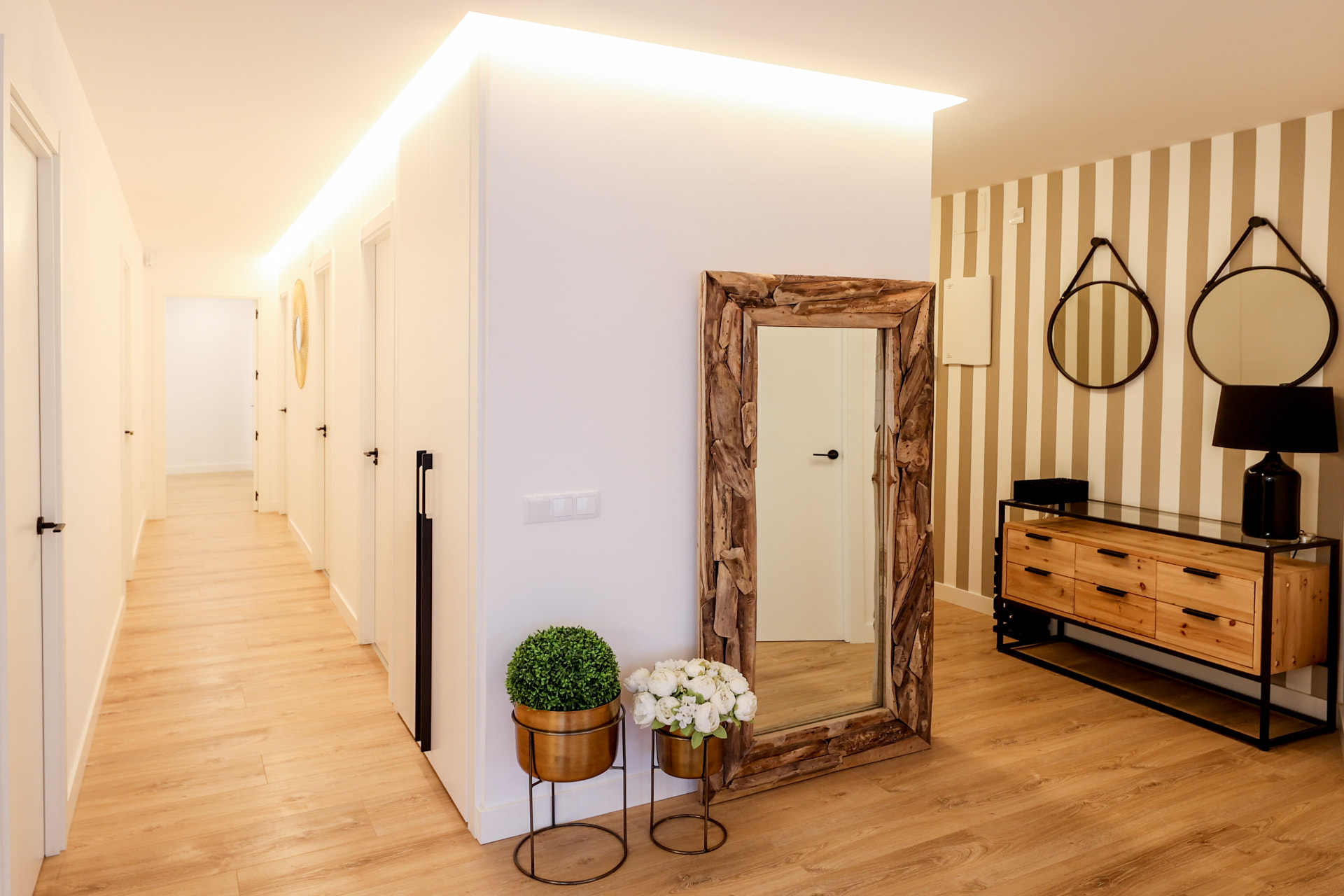Distribuidor reformado con espejo de madera, iluminación indirecta y mobiliario natural
